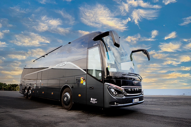 Moderner schwarzer Reisebus von Schatorjé Reisen auf einem offenen Platz bei Sonnenuntergang.